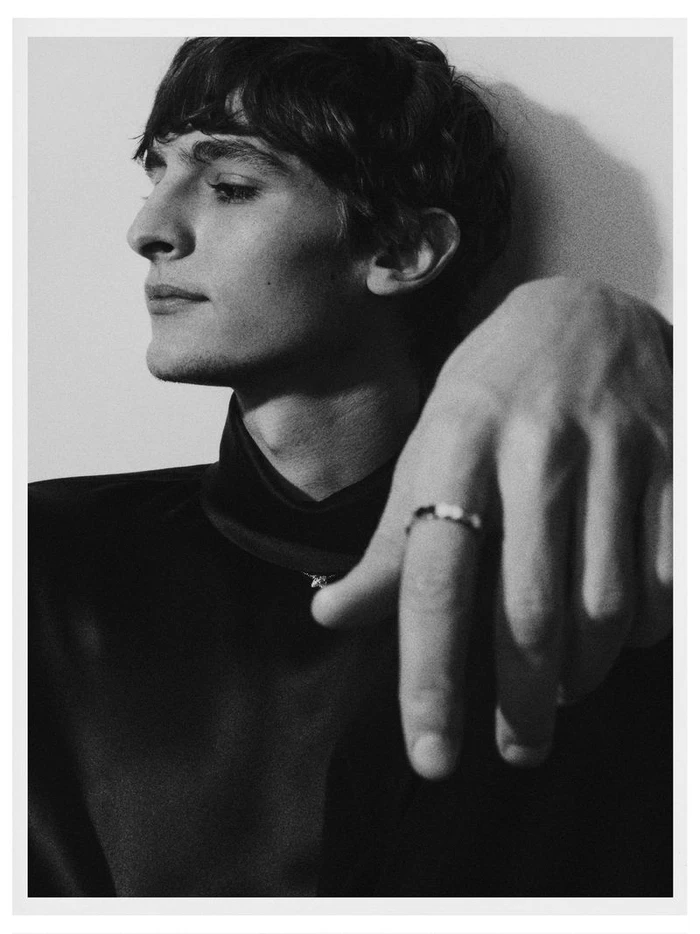 Portrait of male model Vassili Schneider in black top with hand raised against a plain wall for Silhouette Magazine