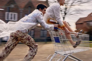 Two men pushing and riding a shopping cart outdoors in a residential area with motion blur background.