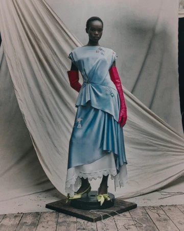 Fashion editorial image featuring an African woman in a light blue dress with red gloves posing in a studio setting.