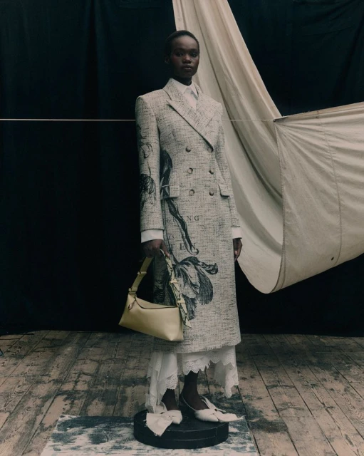 Fashion shot of an African woman posing in a tweed coat dress with a handbag, white tights and heels in an indoor studio setting.