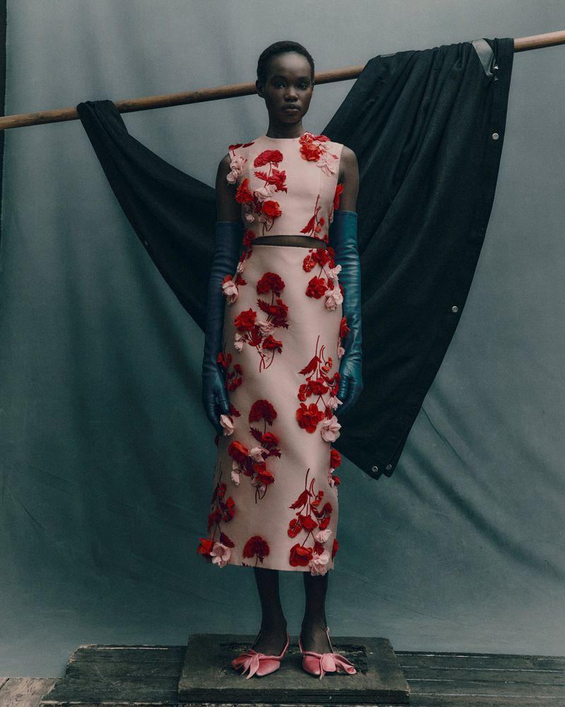 Fashion shoot of Black female model in a blush two-piece dress with red flower appliqués and matching blush heels with blue gloves.