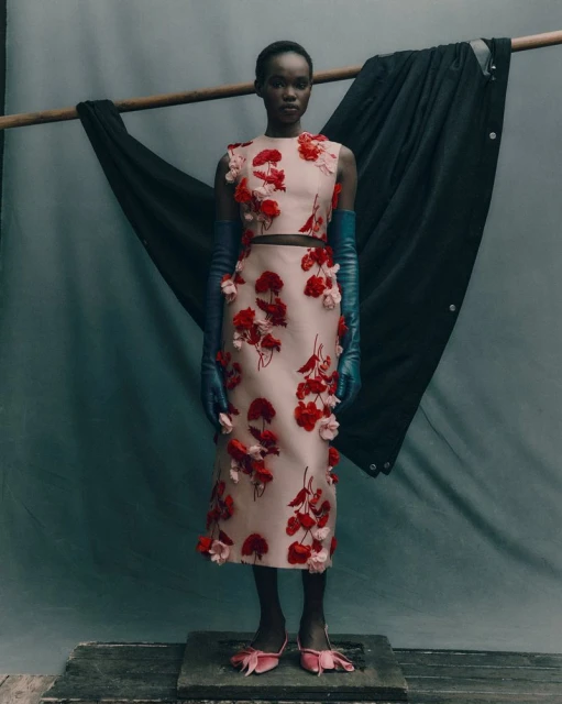 Fashion shoot of Black female model in a blush two-piece dress with red flower appliqués and matching blush heels with blue gloves.
