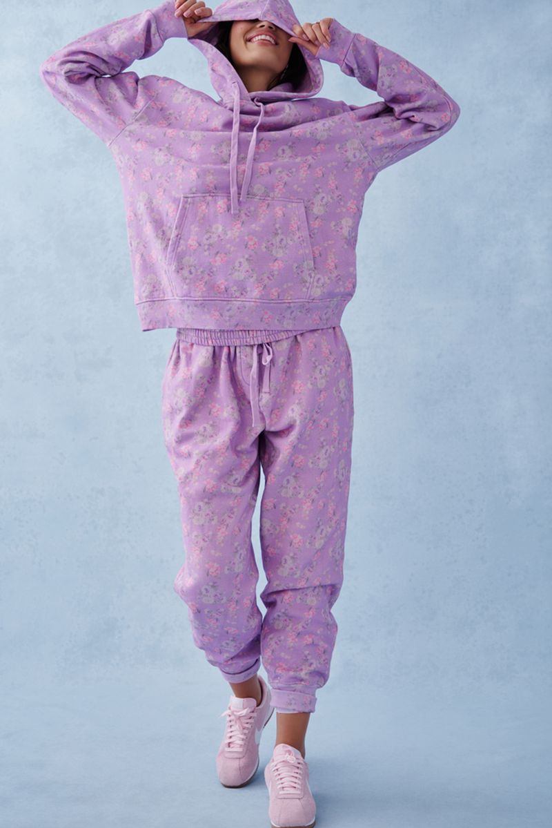 Young woman in a floral print lilac hoodie and sweatpants standing in front of a light blue background in a studio setting.