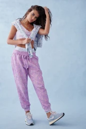 Model in lavender floral sweatpants and pink crop top with a tied sweater against a textured blue backdrop