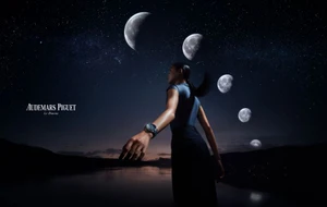 A person wearing a luxury wristwatch stands beneath a night sky filled with multiple moons above a dark landscape.