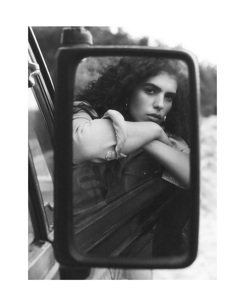 Monochromatic portrait of a woman reflected in a car mirror with a serious expression, capturing a vintage or artistic aesthetic.
