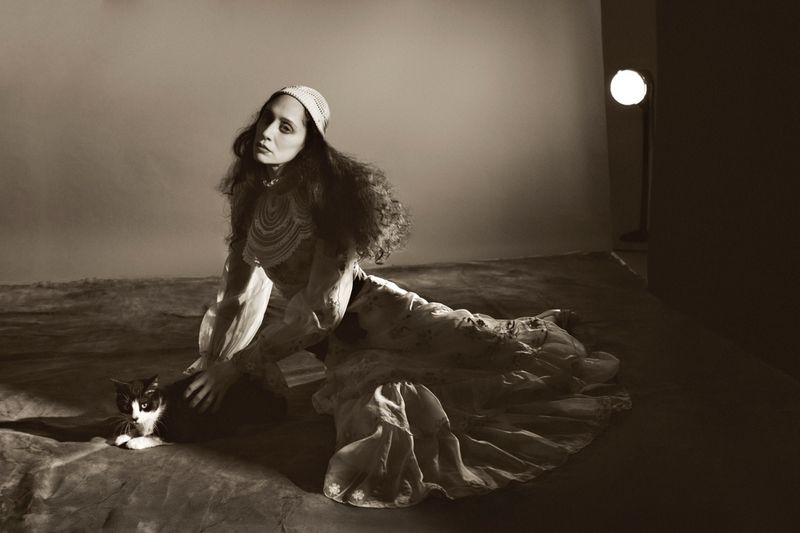 Monochrome portrait of a woman in a patterned dress, seated with a black and white cat in a photo studio setting.