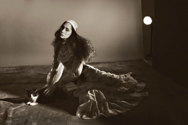 Monochrome portrait of a woman in a patterned dress, seated with a black and white cat in a photo studio setting.