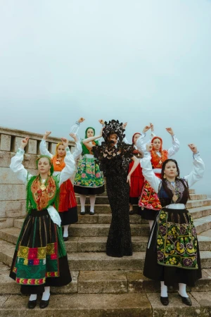 Group of women in traditional dress raising arms in outdoor setting on stone steps, neutral sky, lace details, black and green