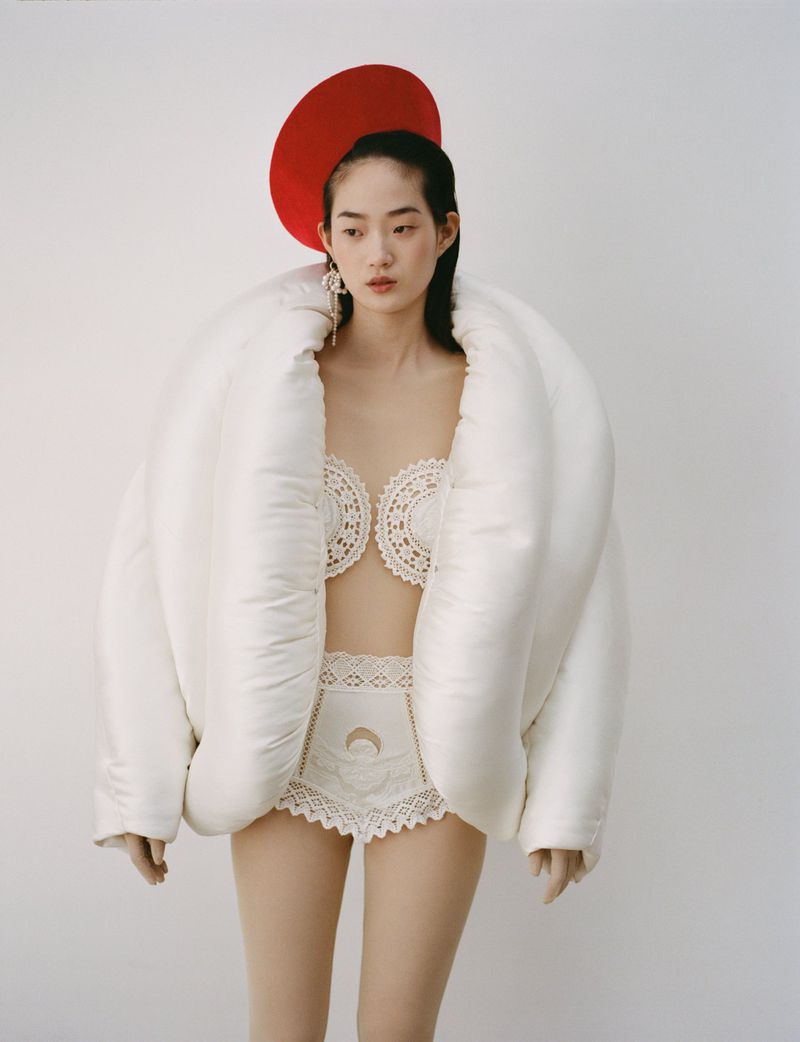 Young Asian woman posing in lingerie with a large white puffer jacket and red beret against a seamless background in a studio shot.