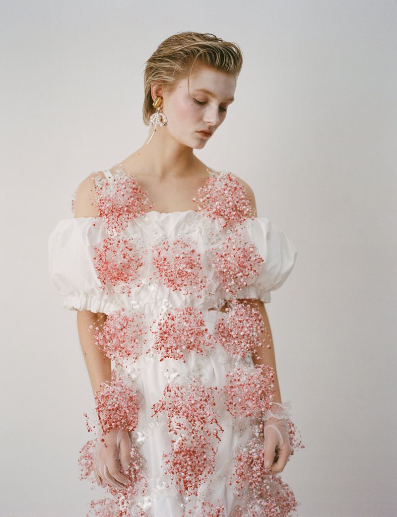 Woman poses in a white gown adorned with pink embellishments, featuring an off-the-shoulder design, captured in a studio setting.