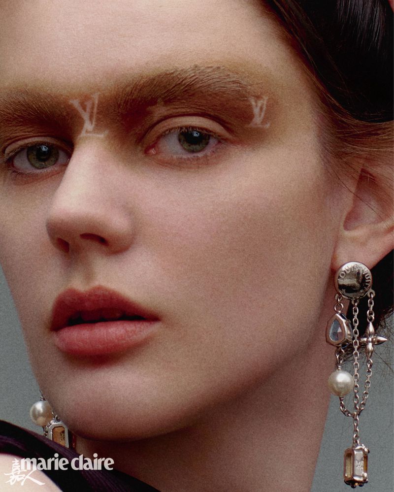 Close-up beauty shot of a woman with a light skin tone, featuring makeup details such as branded eyebrows and statement earrings.