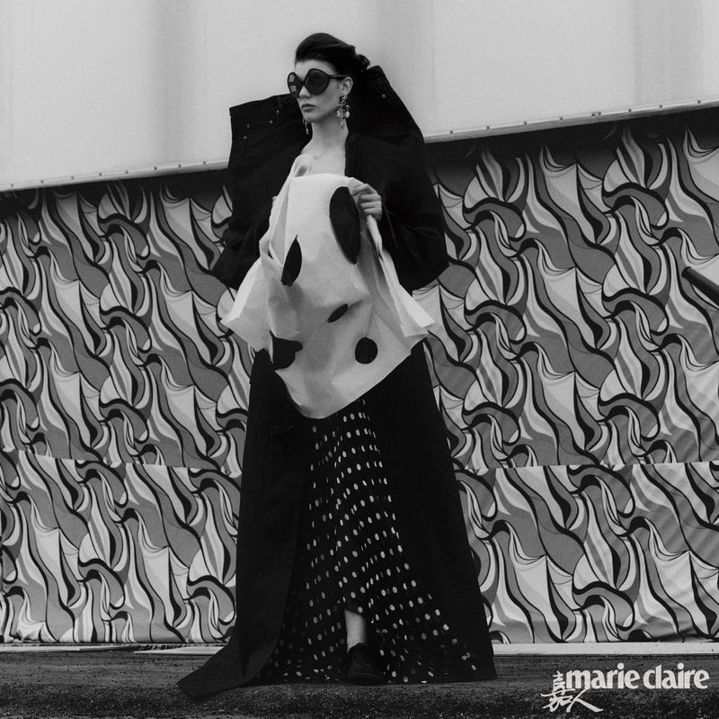 Editorial fashion shot in black and white featuring a female model in an avant-garde outfit with polka dots and an abstract backdrop.