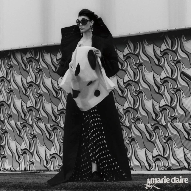 Editorial fashion shot in black and white featuring a female model in an avant-garde outfit with polka dots and an abstract backdrop.