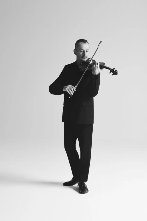 Monochrome full shot of a man in a suit playing the violin with a focused expression in a white studio setting.