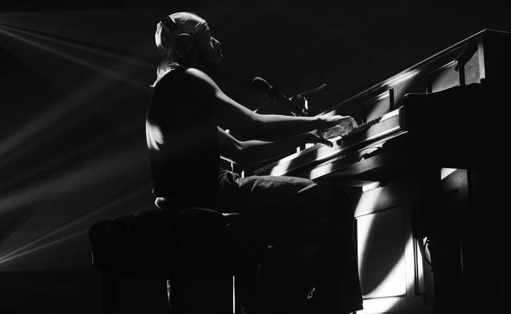 Black and white shot of a musician at a grand piano, with dramatic lighting and a microphone in a dark music hall.