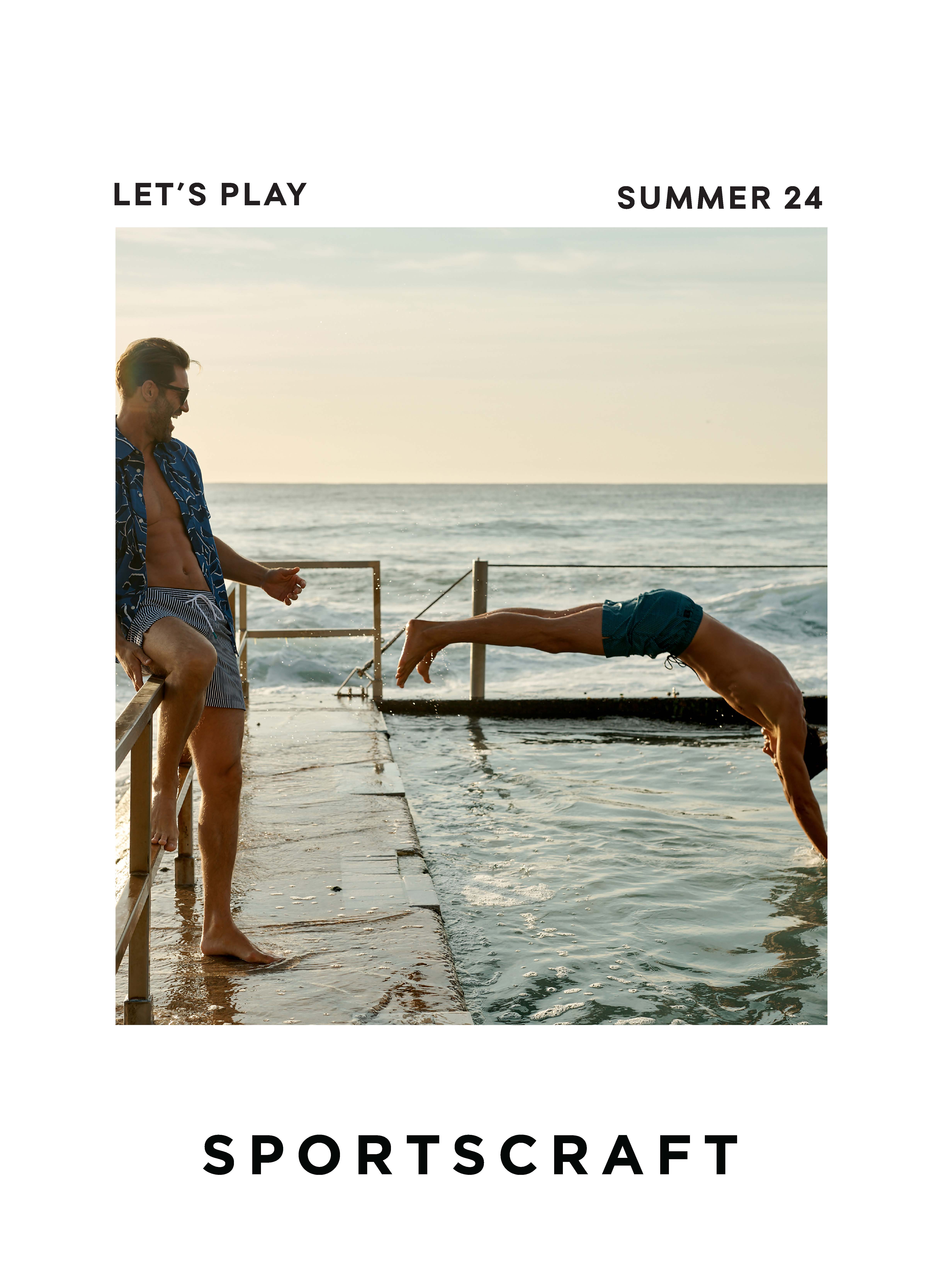 Two men on a seaside concrete pier with one diving into the ocean, showcasing a playful summer vibe with ocean backdrop.
