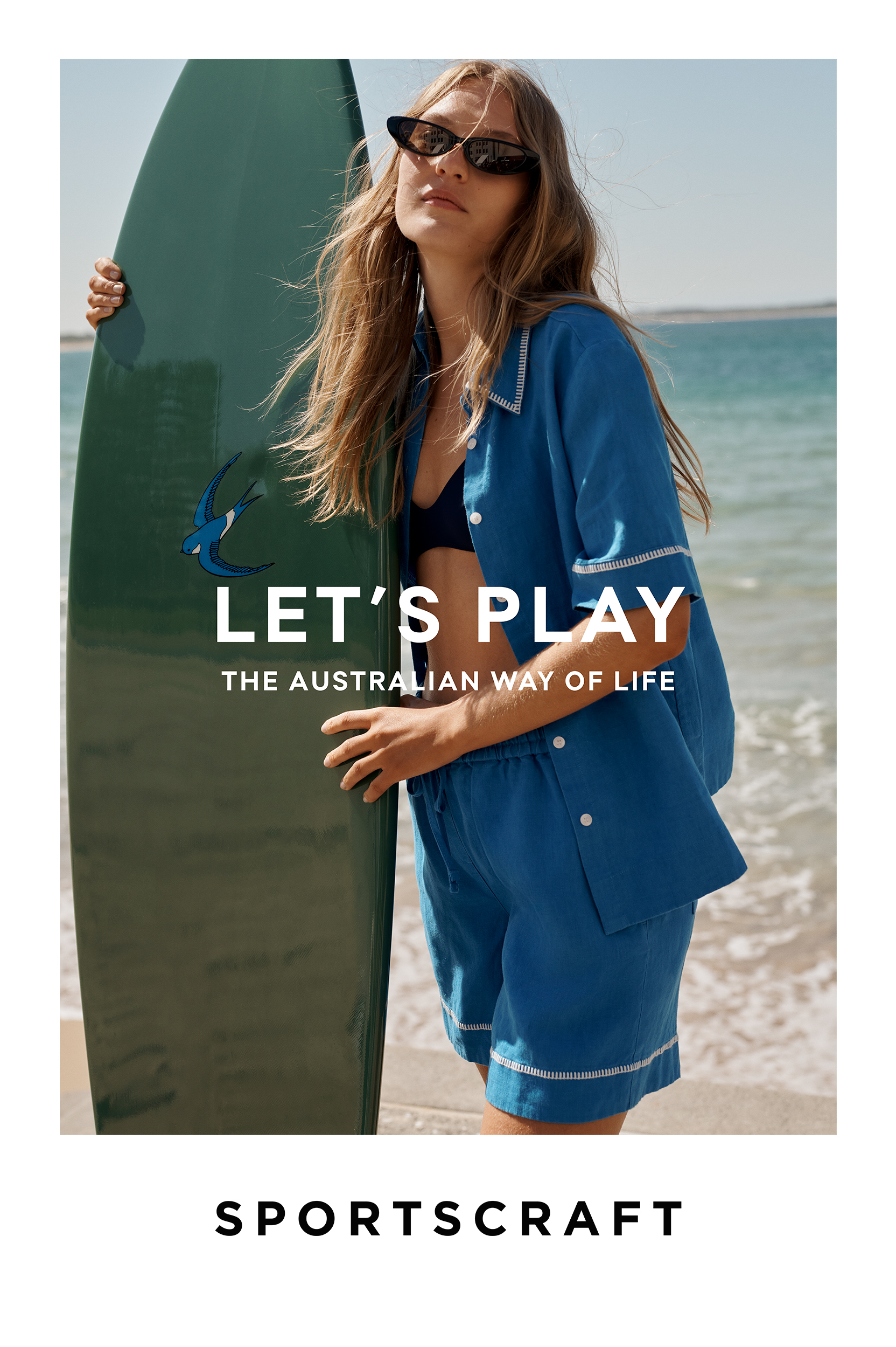 A woman poses with a surfboard on a beach, wearing a blue pajama set and sunglasses against the backdrop of the ocean and sky.