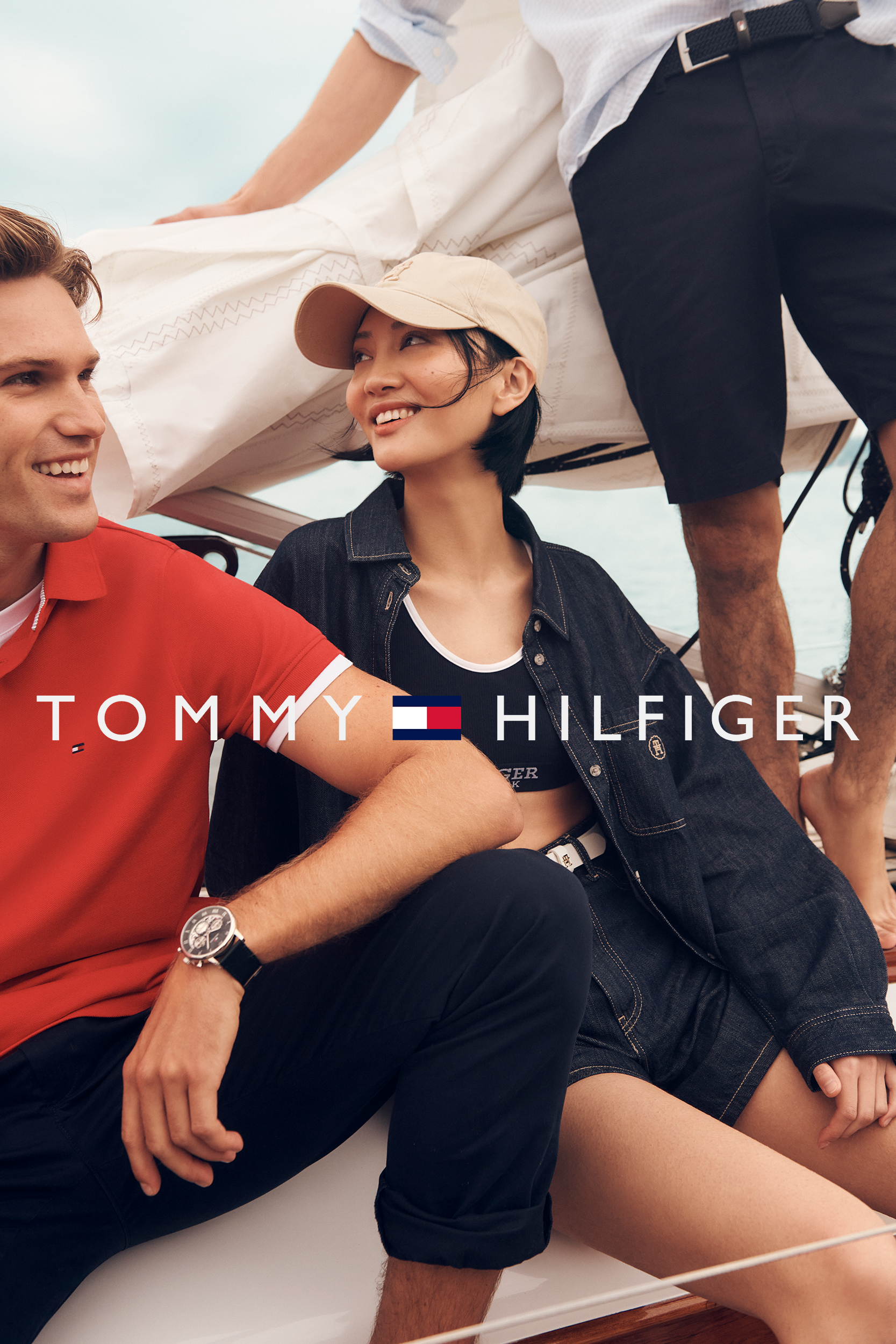 Three people wearing Tommy Hilfiger clothing on a boat. An adult male in a red shirt is smiling and looking at the camera.