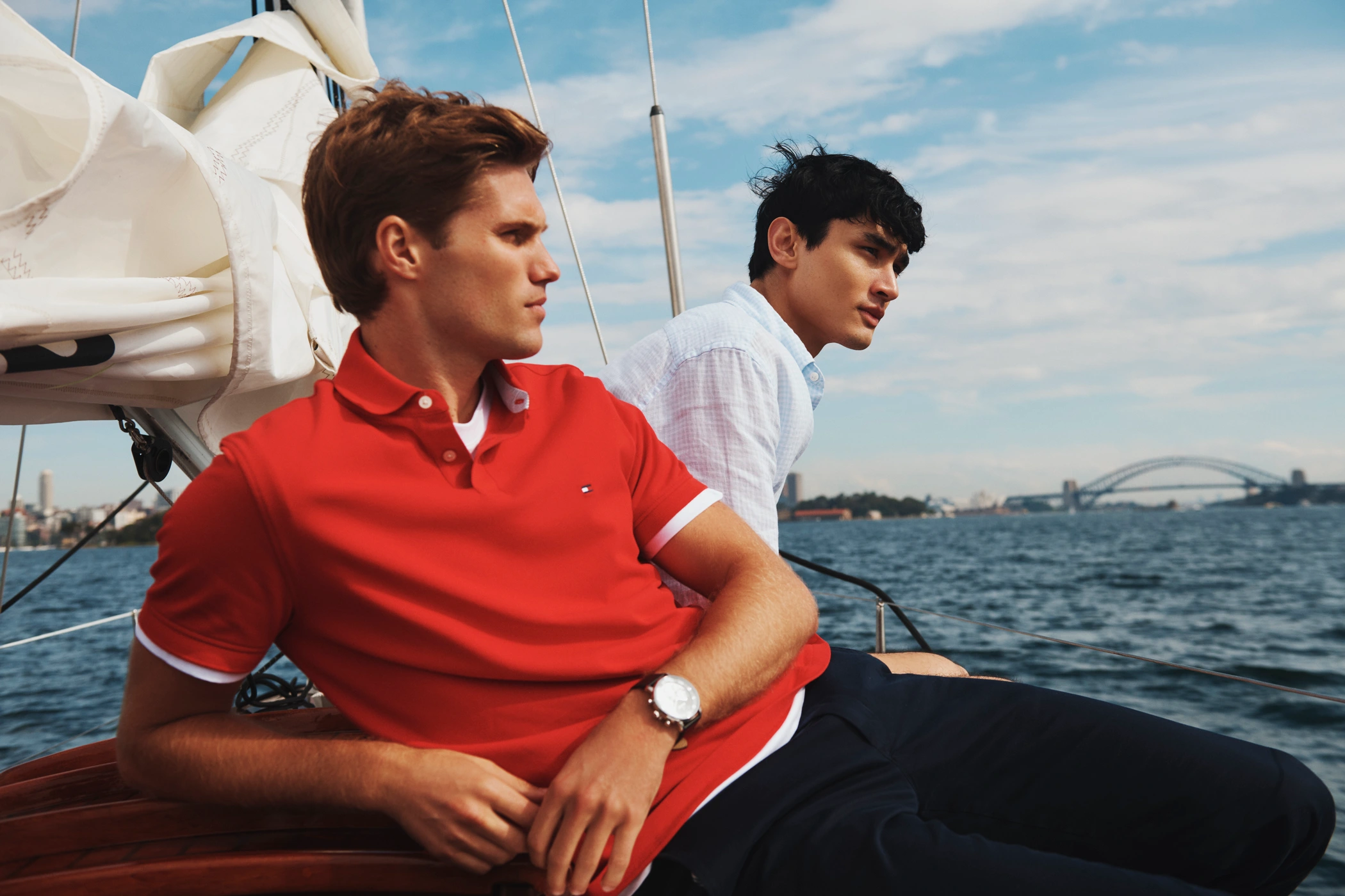 Two men relaxing on a sailboat deck on the water with a bridge in the background for a Tommy Hilfiger campaign