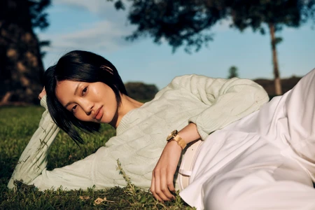 Woman in mint green sweater and white pants lying on grass for Tommy Hilfiger