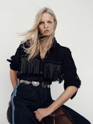 Blonde female model wearing a black fringed shirt and dark denim jeans against a plain white studio background.