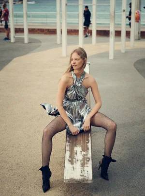 Woman wearing a metallic silver halter dress and black boots sitting outdoors on a playground seesaw