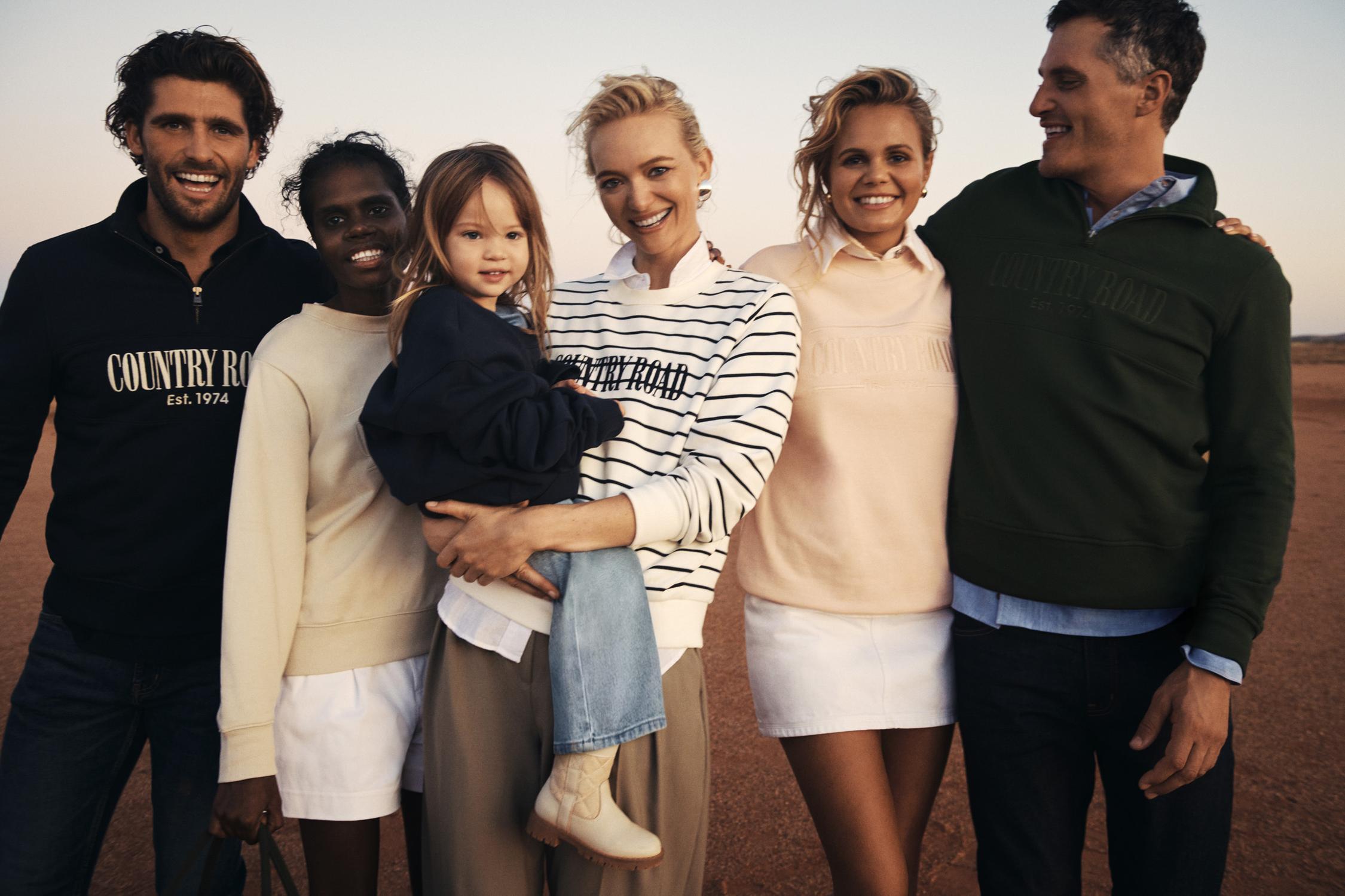 Group shot of six people of diverse ethnicities, including one child, smiling and posing together outdoors in a rural setting.