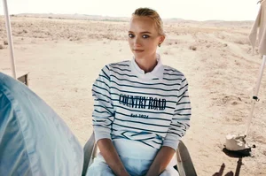 Woman in striped sweatshirt with Country Road branding seated outdoors in a desert landscape for a campaign portrait.