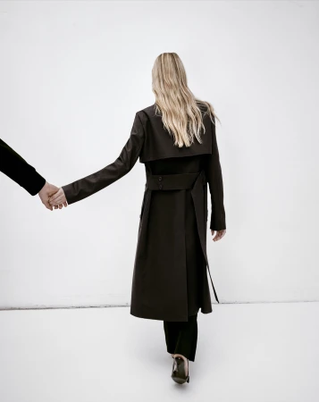 Model with long blonde hair seen from behind wearing a dark brown coat holding hands with another person