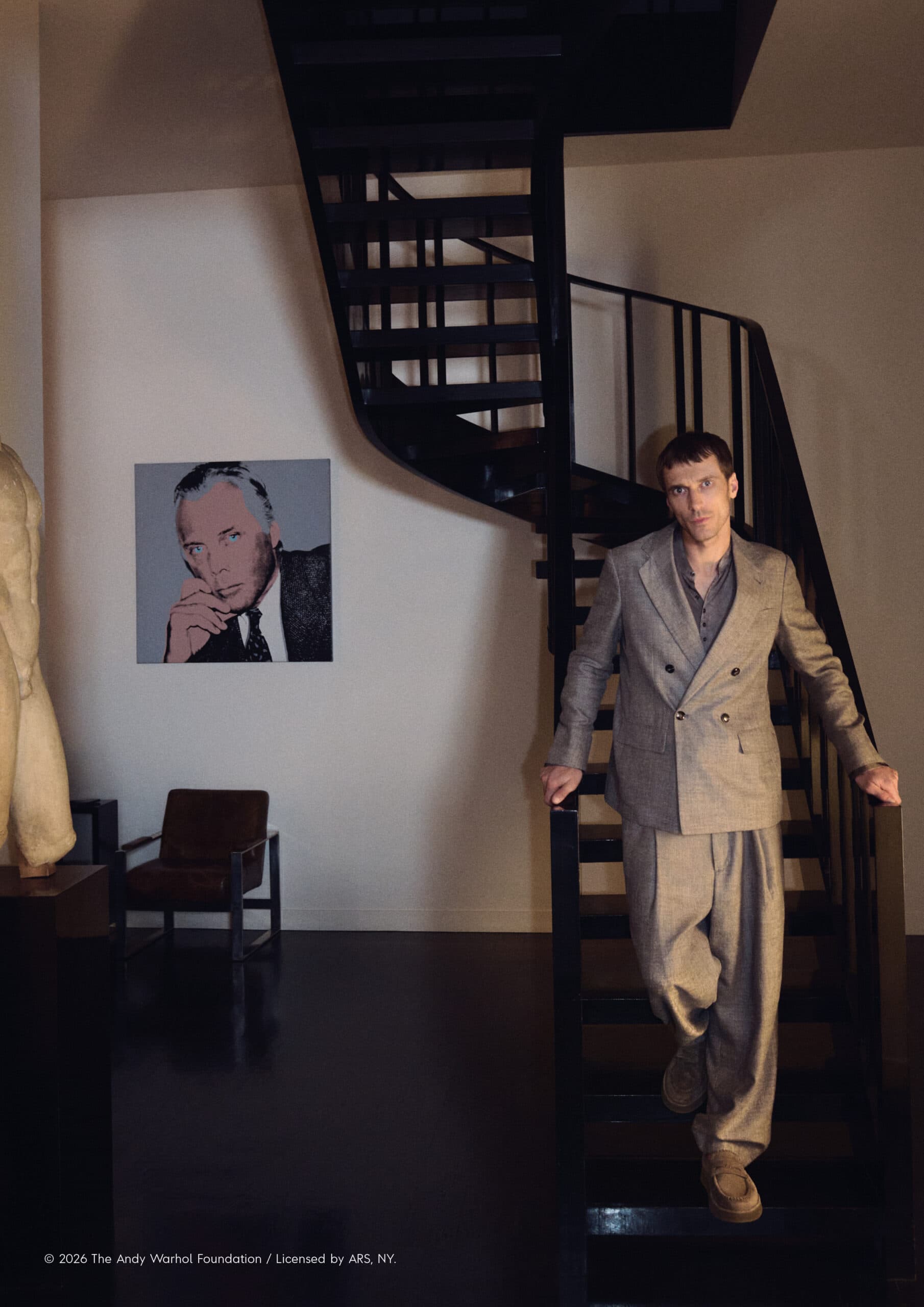 Man in a suit descending black spiral stairs, portrait of a man on the wall, inside a home interior with natural lighting.
