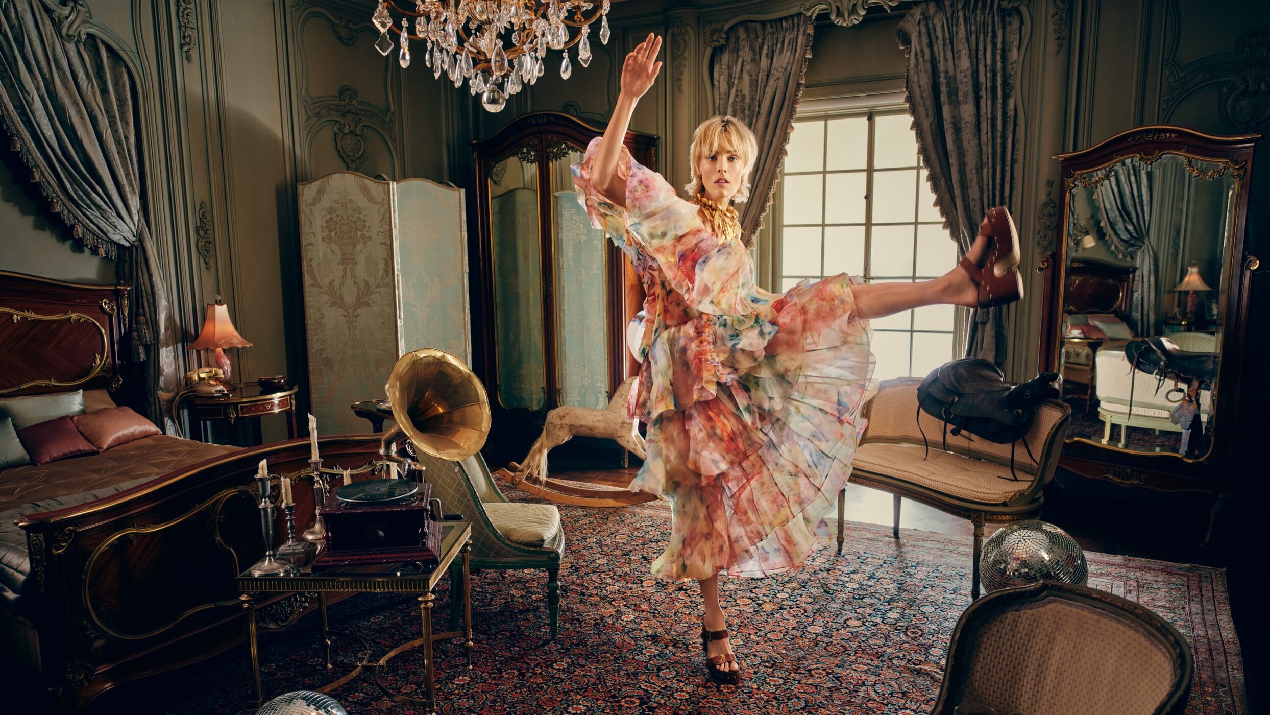 Woman in a ruffled dress strikes a dance pose indoors, with a gramophone, bed, and decorative furnishings enhancing the vintage ambiance.