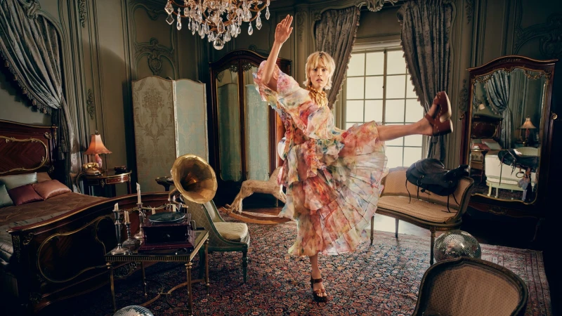 Model in a floral ruffled dress dancing in a lavishly decorated bedroom with antique furniture and a chandelier
