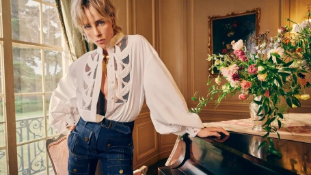Model in white shirt and denim pants leaning on a piano with a floral arrangement for Zimmermann Spring 2026 ad campaign