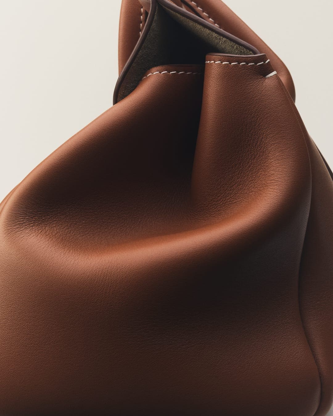 Close-up shot of a brown leather purse with stitching detail, showcasing luxury fashion accessory against a neutral backdrop.