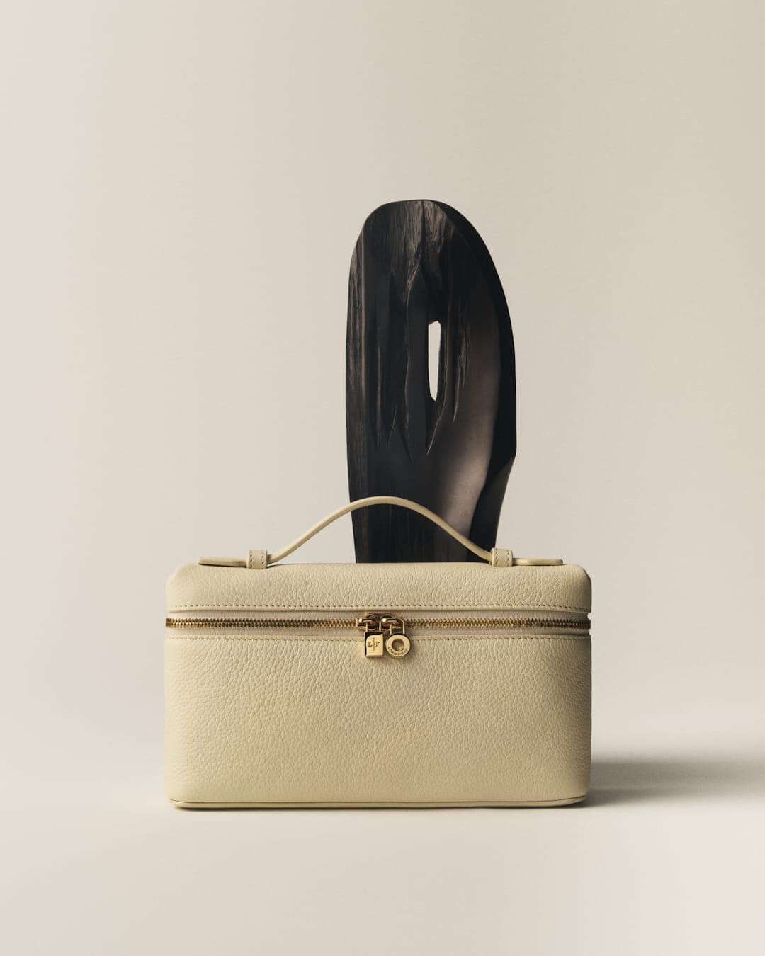 Luxurious cream-colored leather vanity case with gold hardware alongside a dark, abstract geometric sculptural object.
