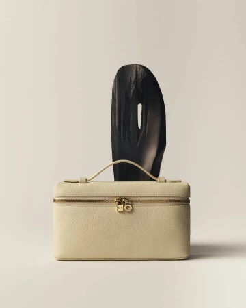 Luxurious cream-colored leather vanity case with gold hardware alongside a dark, abstract geometric sculptural object.