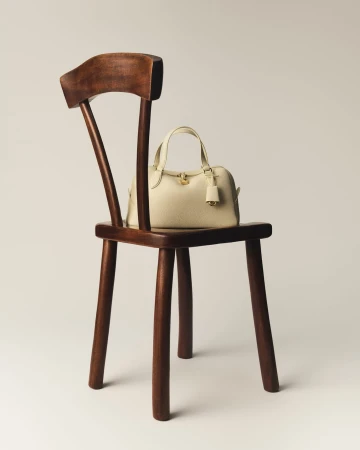 Cream leather handbag resting on a dark polished wooden chair against a plain light background