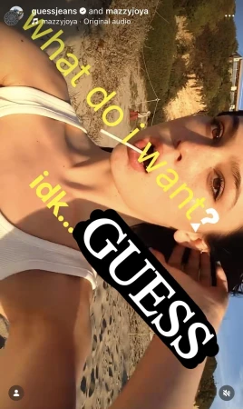 A woman is holding a lollipop on a beach with light-colored sand. She is wearing a white top. Filtered light illuminates the scene.