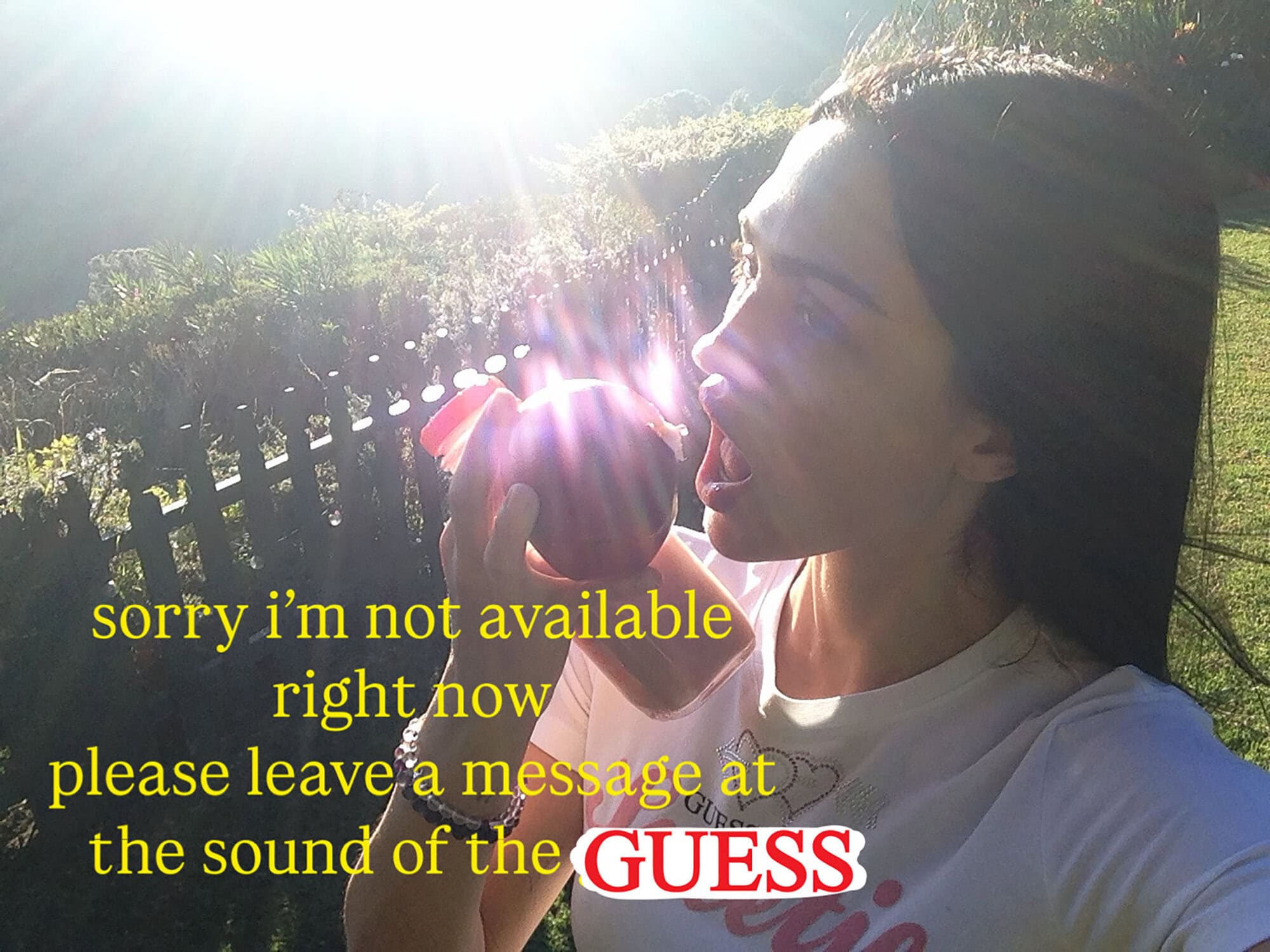 Profile of a brunette woman with mouth open holding a dark red fruit outside with greenery and fence, backlit with the sun shining brightly.