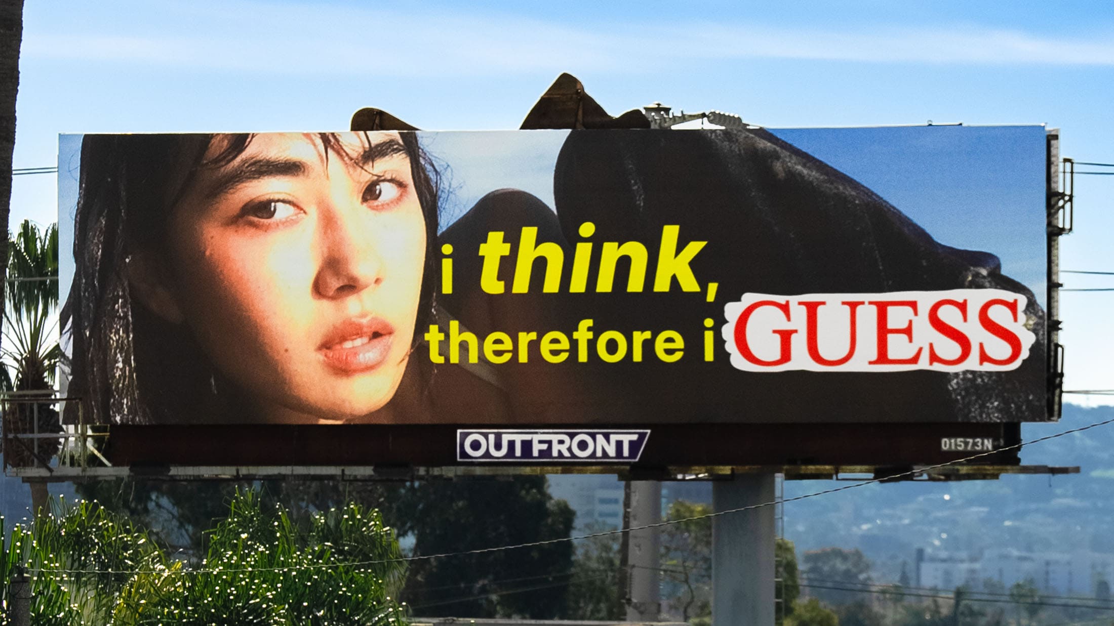 Billboard advertisement with a close up portrait of a woman next to 'I think, therefore I Guess' text with palm trees in the background.