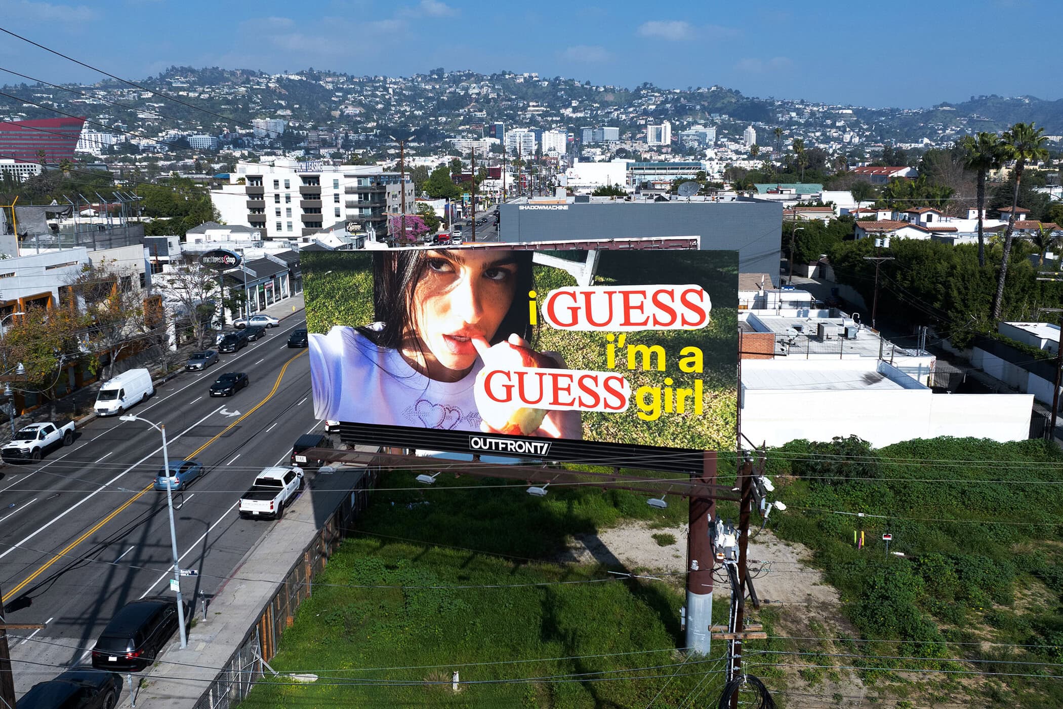 Aerial view of a large urban billboard displaying a Guess Jeans ad overlooking a busy city street and buildings