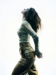 Profile of a woman with long hair wearing a sparkly top and gold trousers against a bright white background