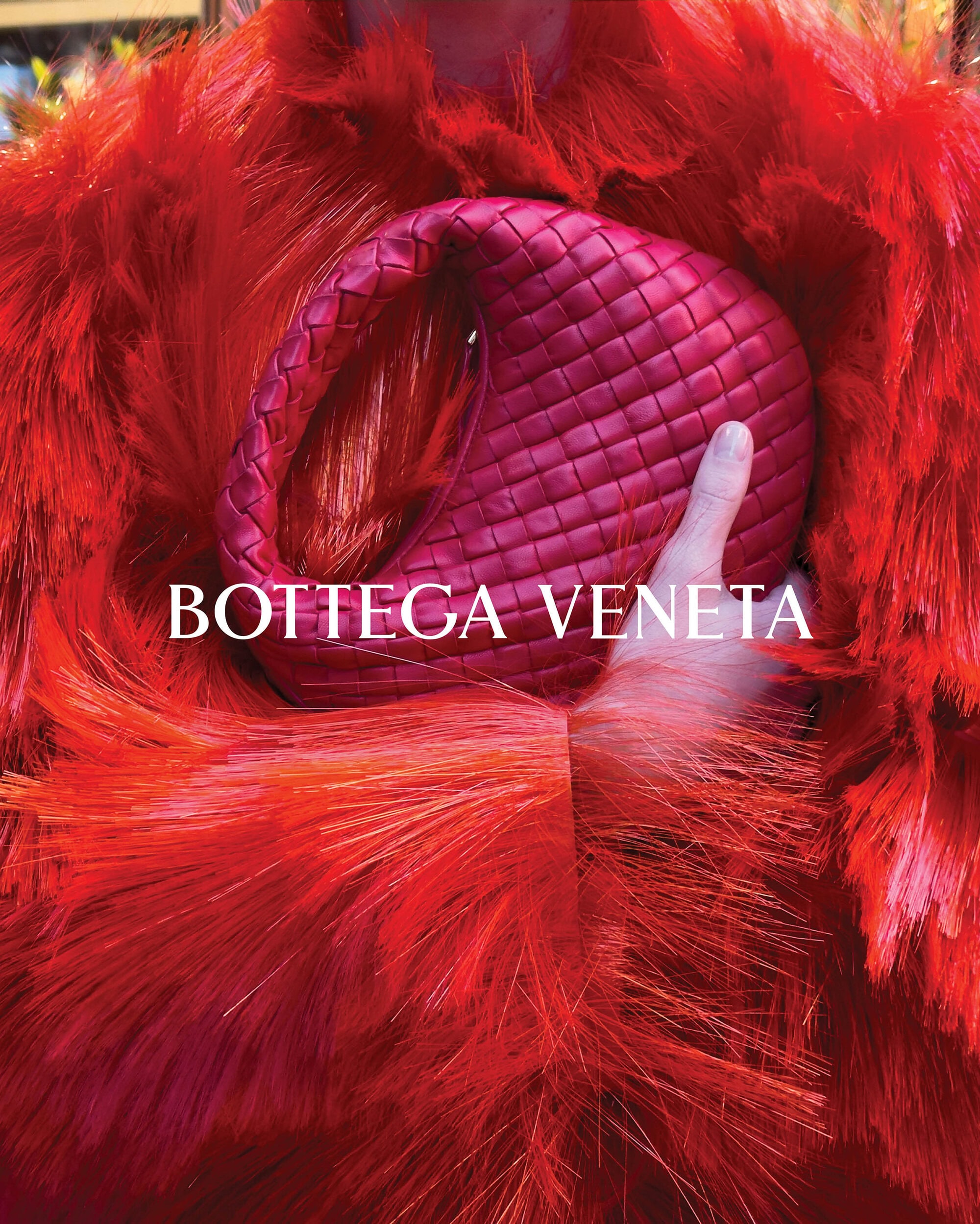 Close-up of a woman with a red feathered collar holding a Bottega Veneta woven red handbag. Fashion and style.