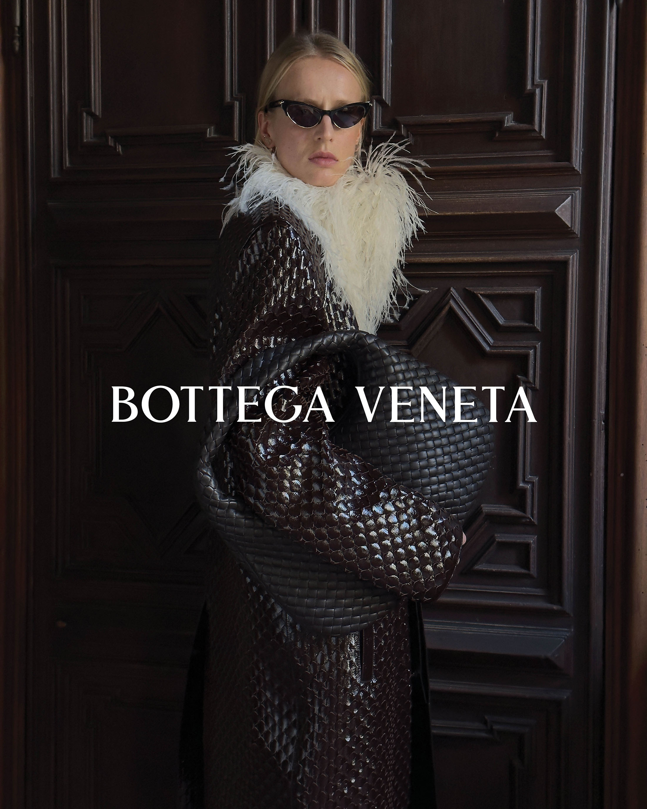 Adult woman with sunglasses and a textured jacket posing in front of a dark wooden door with BOTTEGA VENETA text overlay.