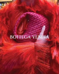 Close-up of a person wearing a textured red fringe coat holding a woven magenta leather handbag for Bottega Veneta