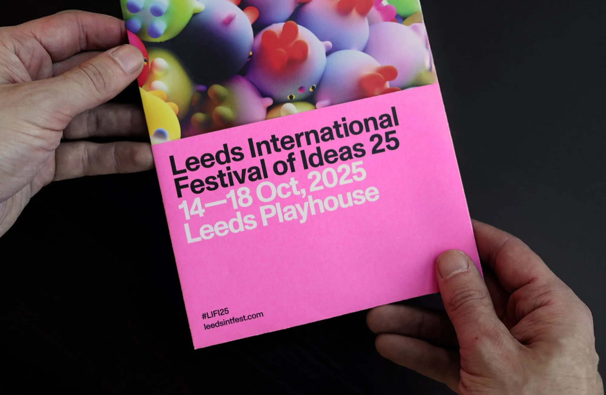 Close-up of a hand holding a promotional pink leaflet advertising the Leeds International Festival of Ideas 25, October 14-18, 2025.