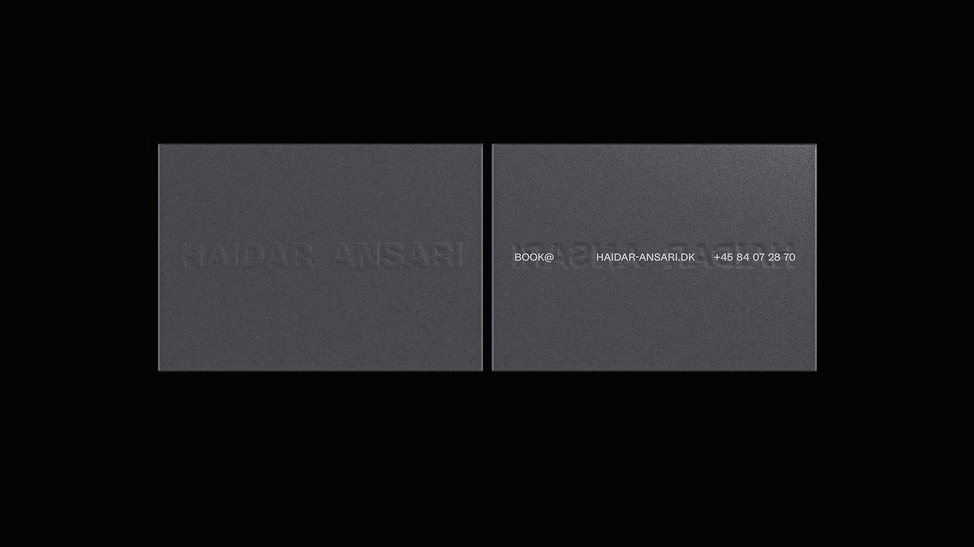 Two dark gray business cards with lightly debossed text on a dark black background, showcasing a minimalist and sophisticated design.