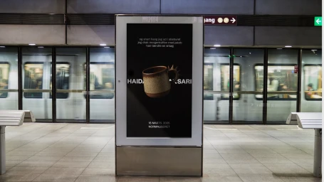 Vertical digital advertising poster featuring a ceramic mug on a black background displayed inside a train station platform.