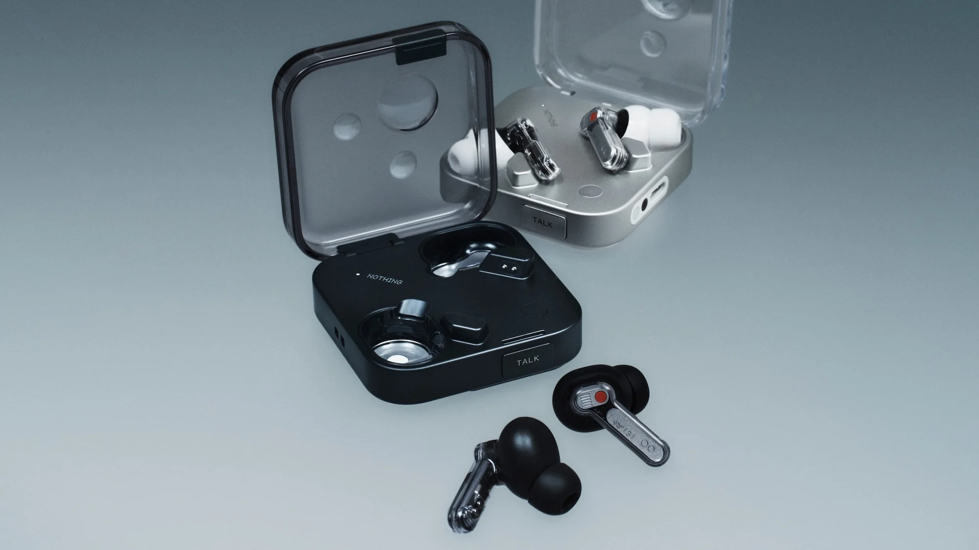 Close-up studio shot of black and silver 'Nothing' brand wireless earbuds inside open cases on gray background showcasing tech design.